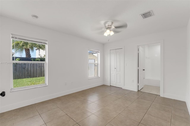 unfurnished bedroom with ceiling fan, light tile patterned floors, ensuite bath, and a closet