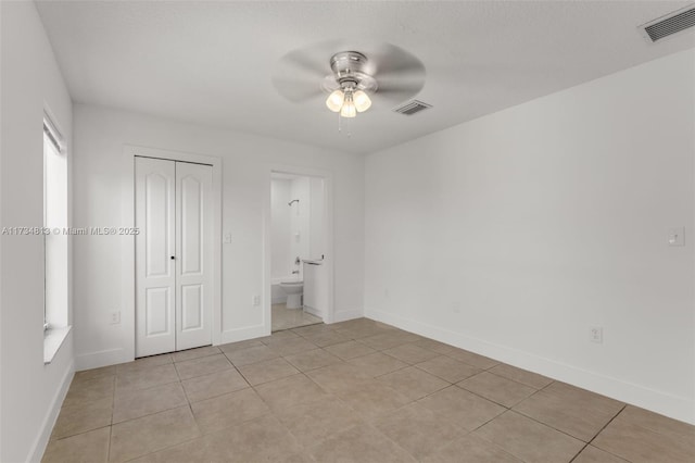 unfurnished bedroom featuring light tile patterned flooring, ceiling fan, ensuite bath, and a closet