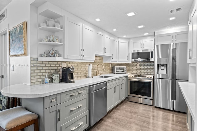 kitchen with sink, a breakfast bar area, stainless steel appliances, light hardwood / wood-style floors, and decorative backsplash