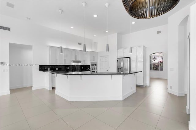 kitchen with stainless steel fridge, a breakfast bar area, a kitchen island with sink, white cabinetry, and a towering ceiling