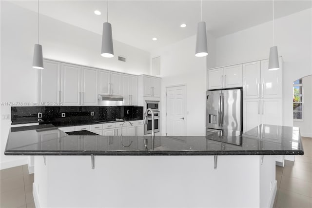 kitchen with hanging light fixtures, dark stone counters, a high ceiling, and appliances with stainless steel finishes