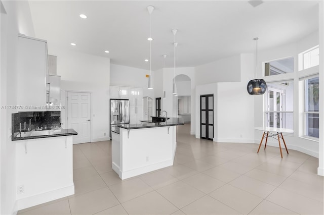 kitchen with white cabinetry, a kitchen island with sink, stainless steel fridge with ice dispenser, and hanging light fixtures