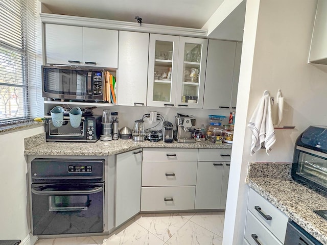 kitchen with light stone counters, black oven, and white cabinets