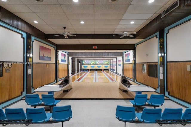 game room featuring a bowling alley, ceiling fan, a paneled ceiling, and wooden walls