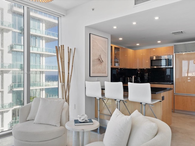 kitchen with light tile patterned floors, backsplash, a kitchen breakfast bar, paneled built in fridge, and light brown cabinets