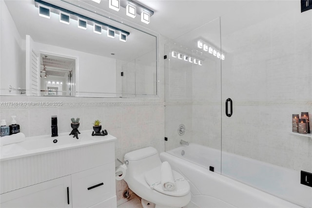 full bathroom featuring bath / shower combo with glass door, tasteful backsplash, tile walls, vanity, and toilet