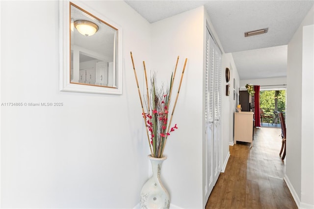 hall with a textured ceiling, wood finished floors, visible vents, and baseboards