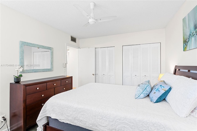 bedroom with multiple closets, visible vents, ceiling fan, and a textured ceiling