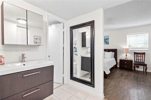 ensuite bathroom with toilet, ensuite bath, two vanities, a textured ceiling, and a sink