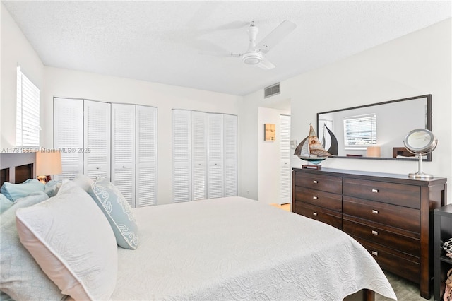 bedroom with multiple closets, visible vents, ceiling fan, a textured ceiling, and multiple windows