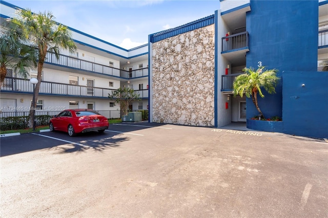 view of building exterior with uncovered parking, central AC unit, and fence