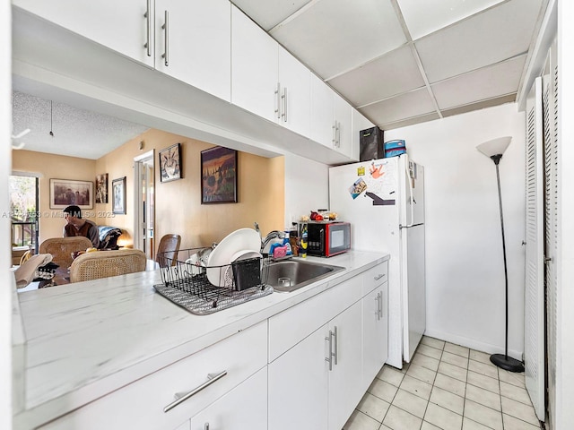 kitchen with light countertops, black microwave, light tile patterned floors, white cabinets, and a drop ceiling