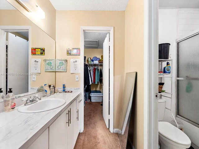 bathroom featuring vanity, toilet, a textured ceiling, and a shower with shower door