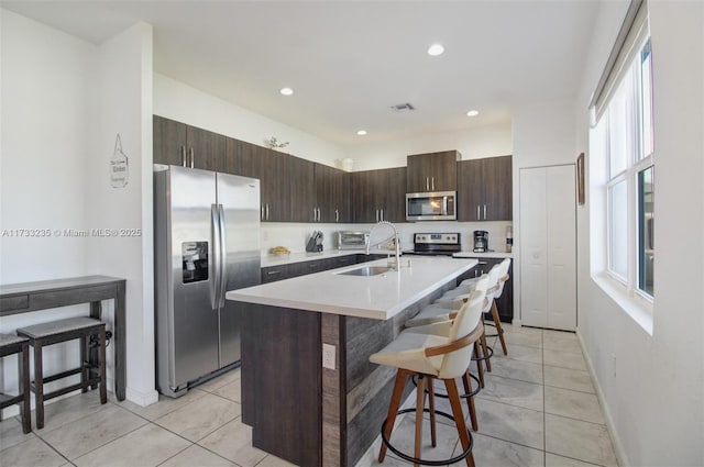 kitchen featuring light tile patterned floors, dark brown cabinets, a kitchen breakfast bar, stainless steel appliances, and an island with sink