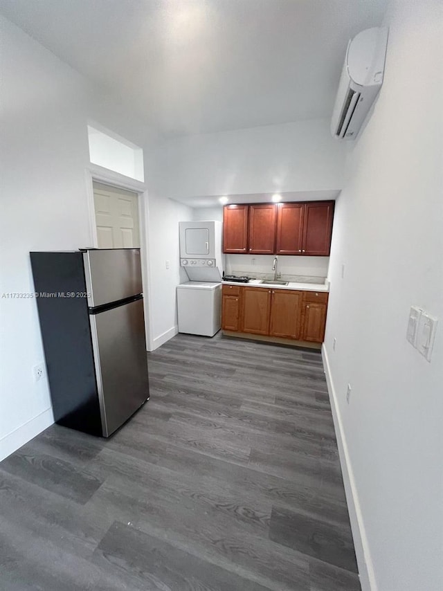 kitchen with dark wood-type flooring, stacked washer / drying machine, sink, an AC wall unit, and stainless steel refrigerator