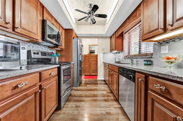 kitchen with sink, tasteful backsplash, light wood-type flooring, appliances with stainless steel finishes, and a raised ceiling