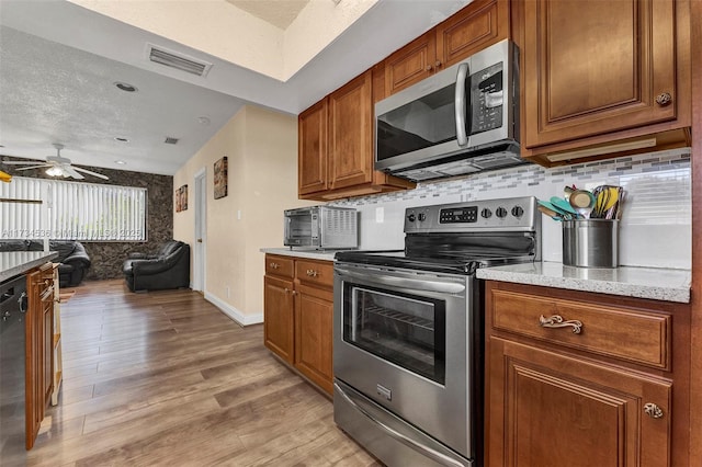 kitchen with ceiling fan, appliances with stainless steel finishes, tasteful backsplash, light hardwood / wood-style floors, and a textured ceiling