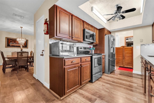 kitchen featuring appliances with stainless steel finishes, decorative light fixtures, light hardwood / wood-style floors, and a textured ceiling