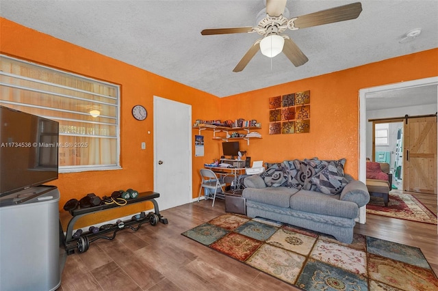 living room featuring ceiling fan, a barn door, hardwood / wood-style floors, and a textured ceiling