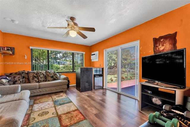 living room with wood-type flooring, a wall mounted AC, a textured ceiling, and ceiling fan