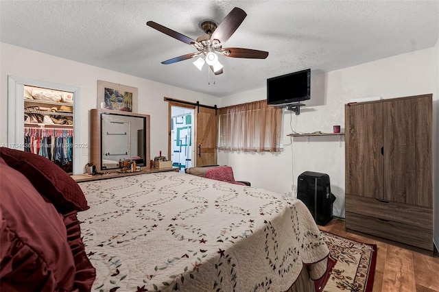 bedroom featuring a barn door, a spacious closet, a textured ceiling, and ceiling fan