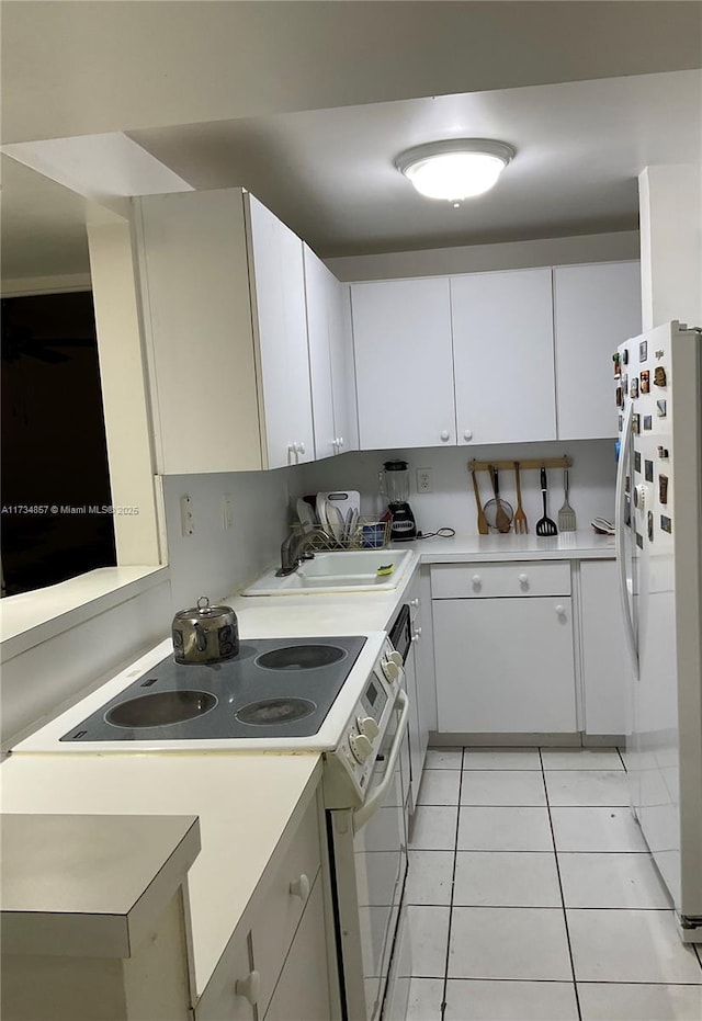 kitchen with electric stove, sink, light tile patterned floors, white cabinetry, and white refrigerator