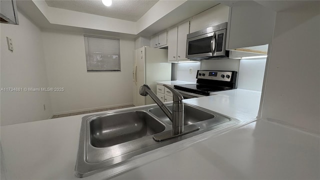 kitchen with sink, white cabinetry, stainless steel appliances, a tray ceiling, and a textured ceiling