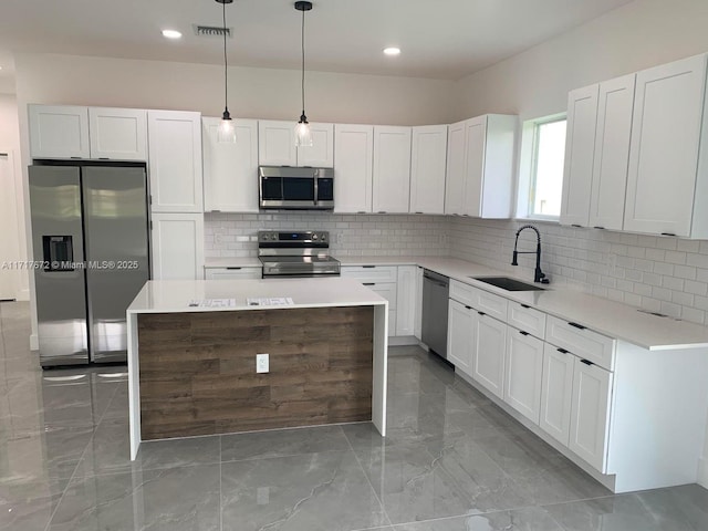 kitchen featuring sink, decorative light fixtures, a kitchen island, stainless steel appliances, and white cabinets