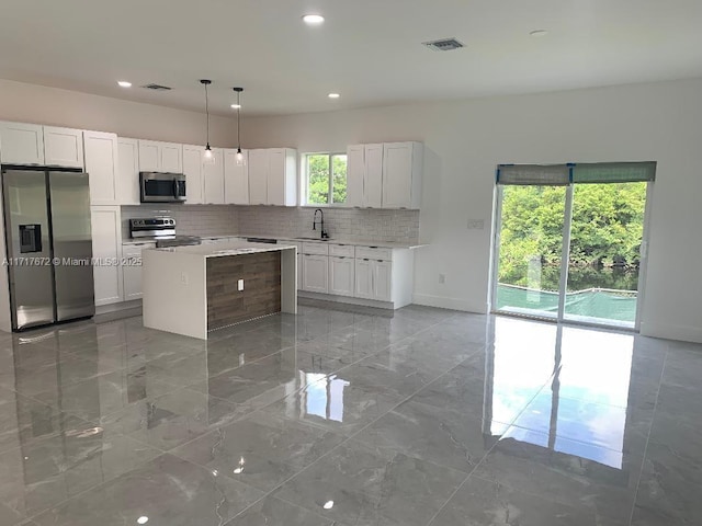 kitchen with appliances with stainless steel finishes, pendant lighting, white cabinets, backsplash, and a center island