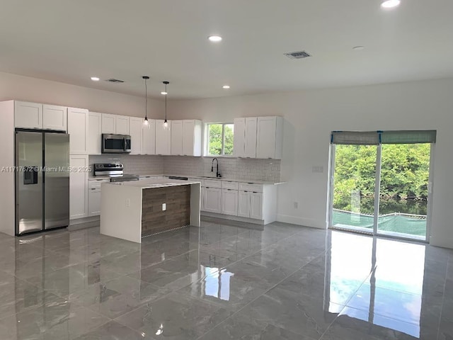 kitchen with pendant lighting, sink, white cabinetry, stainless steel appliances, and a kitchen island