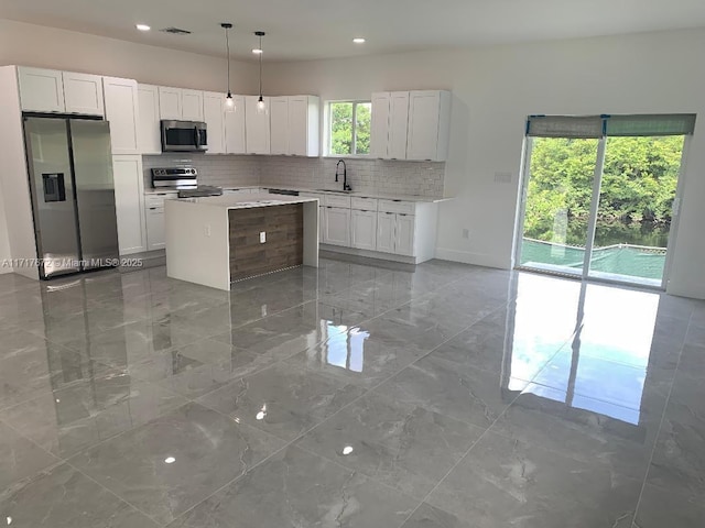 kitchen with sink, appliances with stainless steel finishes, white cabinetry, a center island, and decorative light fixtures