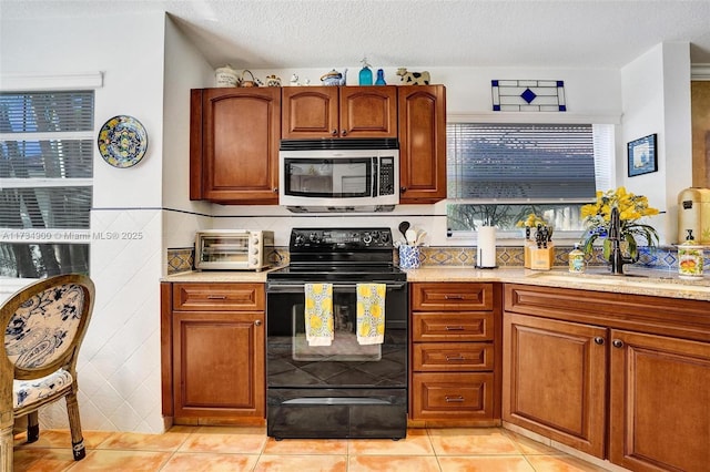 kitchen featuring tile walls, black electric range oven, light tile patterned floors, and a textured ceiling