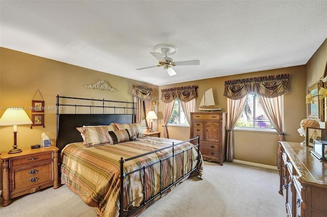 bedroom featuring multiple windows, light colored carpet, a textured ceiling, and ceiling fan