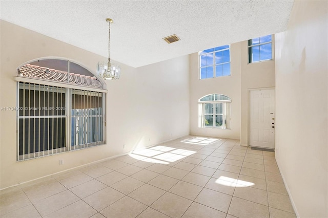 tiled spare room featuring a textured ceiling, a chandelier, and a high ceiling