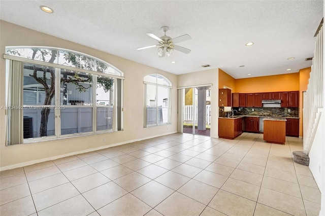 kitchen featuring light tile patterned flooring, decorative backsplash, a center island, ceiling fan, and a textured ceiling