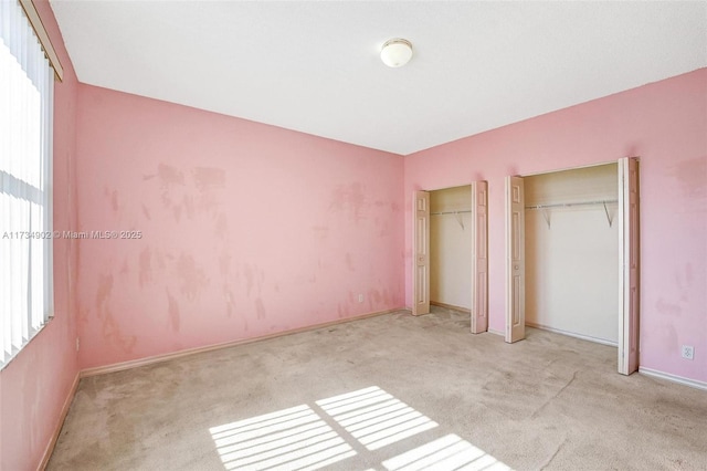 unfurnished bedroom featuring multiple closets, light carpet, and multiple windows