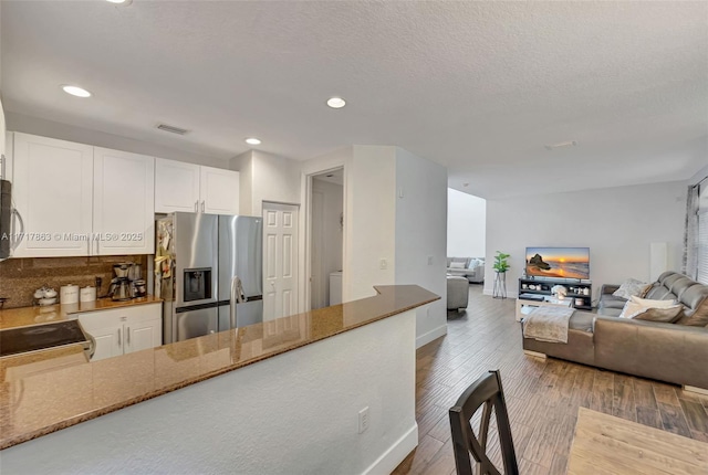 kitchen featuring dark wood-type flooring, light stone counters, a textured ceiling, appliances with stainless steel finishes, and white cabinets