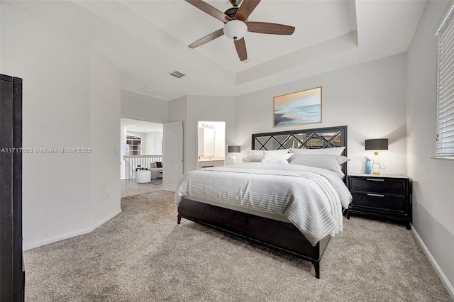 bedroom featuring light carpet, connected bathroom, a tray ceiling, and ceiling fan