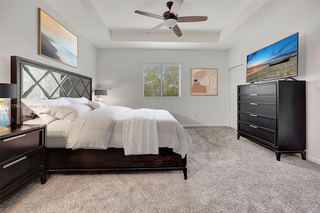 carpeted bedroom with ceiling fan and a tray ceiling