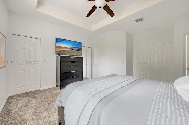 bedroom with a raised ceiling, light colored carpet, and ceiling fan