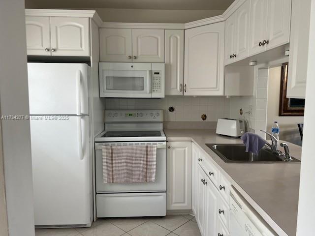 kitchen with sink, white appliances, light tile patterned floors, white cabinetry, and decorative backsplash