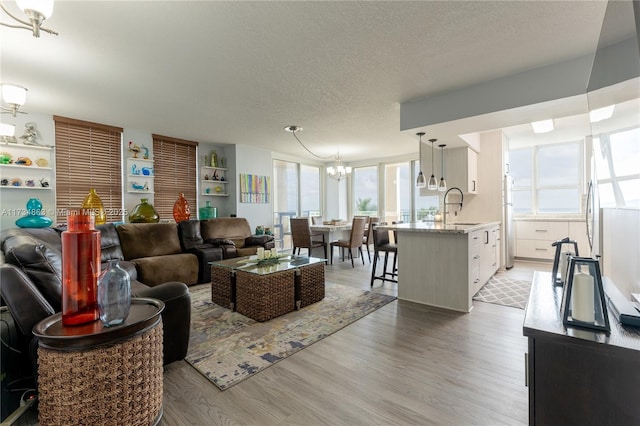 living room with a notable chandelier, sink, a textured ceiling, and light hardwood / wood-style floors