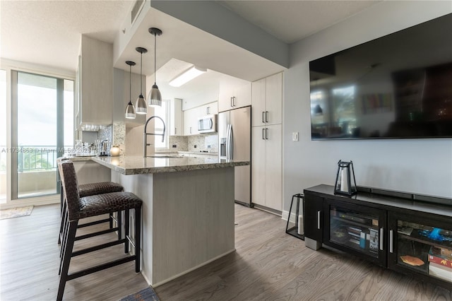 kitchen featuring pendant lighting, sink, stainless steel appliances, a kitchen bar, and kitchen peninsula