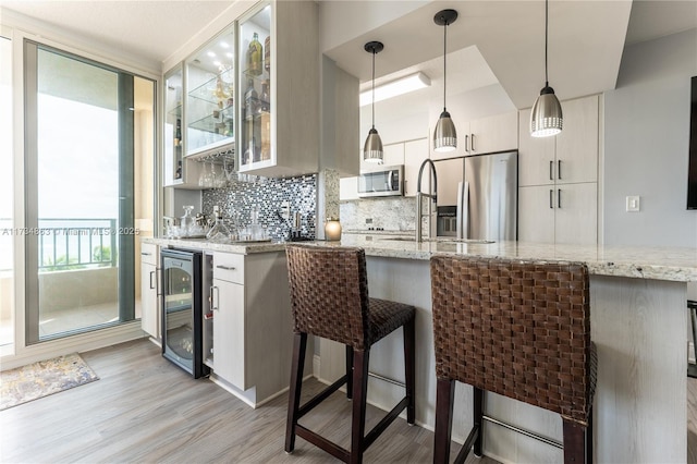 kitchen with pendant lighting, white cabinetry, wine cooler, stainless steel appliances, and light stone countertops