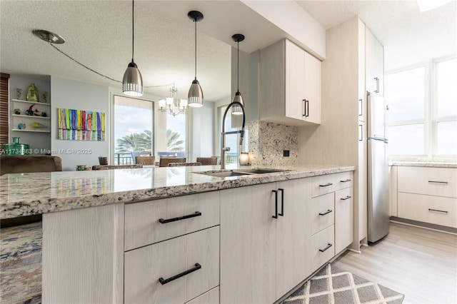 kitchen featuring sink, refrigerator, white cabinetry, hanging light fixtures, and light stone countertops