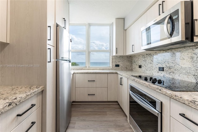 kitchen with light stone counters, a textured ceiling, light wood-type flooring, appliances with stainless steel finishes, and decorative backsplash