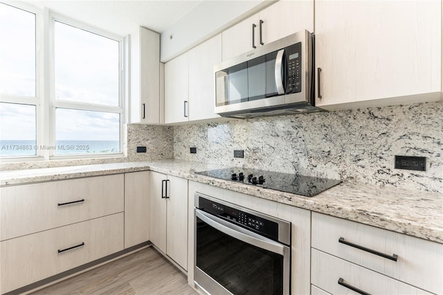 kitchen with light stone countertops, appliances with stainless steel finishes, light wood-type flooring, and decorative backsplash