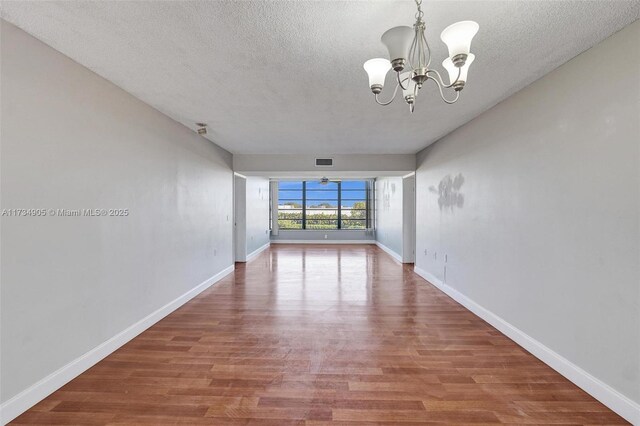 unfurnished room with wood-type flooring, a notable chandelier, and a textured ceiling