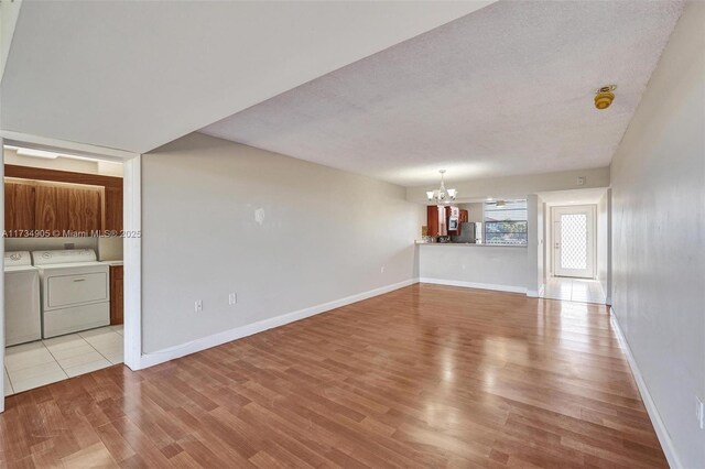 unfurnished living room with washer and clothes dryer, light hardwood / wood-style floors, a textured ceiling, and a notable chandelier