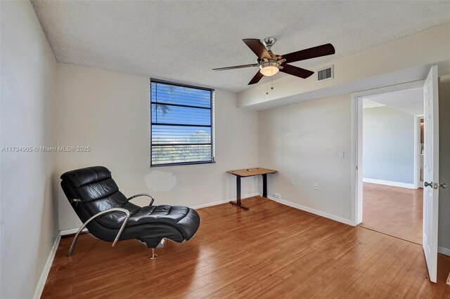 sitting room with hardwood / wood-style flooring, ceiling fan, and a textured ceiling